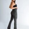Modelo femenino de perfil, modelando un jean oxford o flare color negro nevado con faja, resaltando el calce colombiano que realza la cola