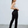 Modelo femenino modelando de perfil, un jean clasico tiro alto recto straight color negro con calce colombiano que levanta la cola
