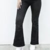 Mujer posando con jean clásico Oxford negro localizado acampanado y botas blancas, vista de frente.