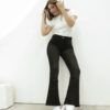 Mujer de pie con jean clásico Oxford negro localizado, camiseta blanca y botas blancas, en ambiente minimalista.