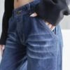 Primer plano de jeans baggy denim azul con efecto gastado y detalles de bigotes. Mano femenina dentro del bolsillo.