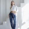 Mujer usando jeans mom fit azul oscuro con crop top blanco y botas blancas, en ambiente blanco con luz natural.