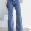 Mujer con jeans wide leg celeste nevado y botas blancas, posando con una mano en el bolsillo sobre fondo blanco.