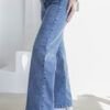 Vista lateral de jean wide leg celeste nevado, con bota blanca y remera blanca entallada.