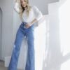 Mujer de cuerpo entero luciendo jeans wide leg celeste nevado y top blanco, posando en escaleras blancas.
