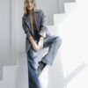 Mujer sentada con blazer gris y jeans wide leg azul óxido, posando con luz suave en interior blanco.