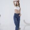 Modelo posando con los brazos levantados mientras viste un jean cargo azul de tiro medio y calzado deportivo, en estudio blanco.