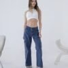 Modelo joven vistiendo un jean cargo azul denim tiro medio con bolsillos laterales, en un ambiente minimalista de estudio con fondo blanco.