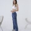 Perfil lateral de mujer joven luciendo un jean cargo azul con bolsillos amplios y costuras visibles, en un estudio de fondo blanco.