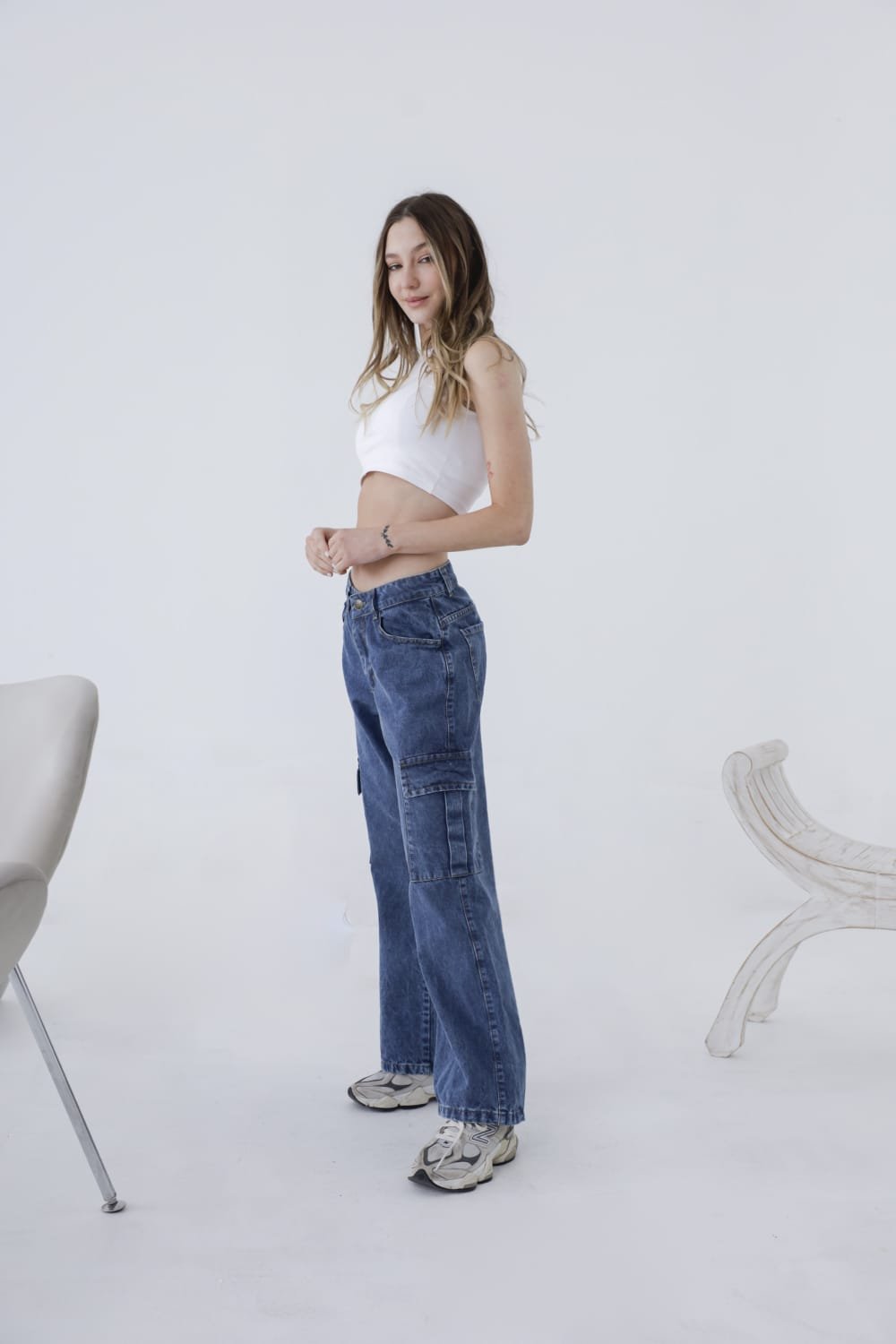 Perfil lateral de mujer joven luciendo un jean cargo azul con bolsillos amplios y costuras visibles, en un estudio de fondo blanco.