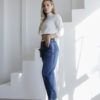Vista lateral de jeans mom fit azul oscuro, con crop top blanco y botas blancas de taco alto.
