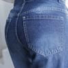 Primer plano del bolsillo trasero de un jean mom fit azul con etiqueta de cuero "FLEX DENIM" y costuras claras.