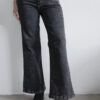 Modelo luciendo jean clásico wide leg negro nevado con top beige ajustado y botas negras de taco.