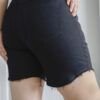 Vista trasera de bermuda denim negro tiro alto con ruedo desflecado y bolsillos clásicos, en modelo femenina.