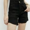 Mujer posando con bermuda denim negro tiro alto, ruedo desflecado y top ajustado negro.