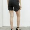 ista trasera de bermuda denim negro nevado con ruedo desflecado y bolsillos clásicos, en modelo femenina.