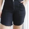 Mujer usando bermuda denim negro liso, tiro alto con ruedo desflecado y bolsillos delanteros, combinada con remera blanca sin mangas.