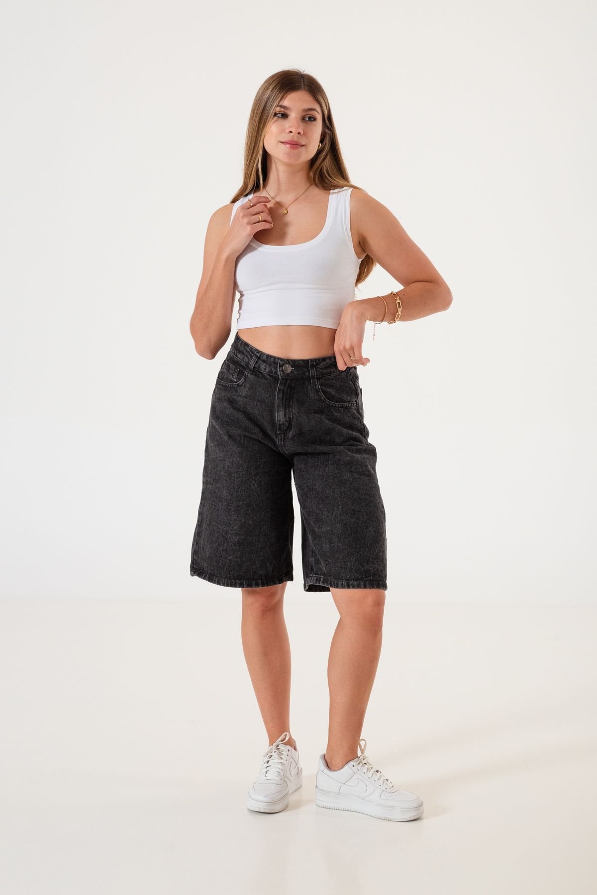 Mujer de pie usando bermuda ancha negra nevado, con crop top blanco y accesorios dorados.