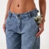 Mujer de pie luciendo jeans baggy celeste nevado en plano completo, combinados con zapatillas blancas y top corto.