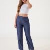 Mujer sonriendo luciendo pantalón recto de twill azul con sandalias negras y crop top blanco.