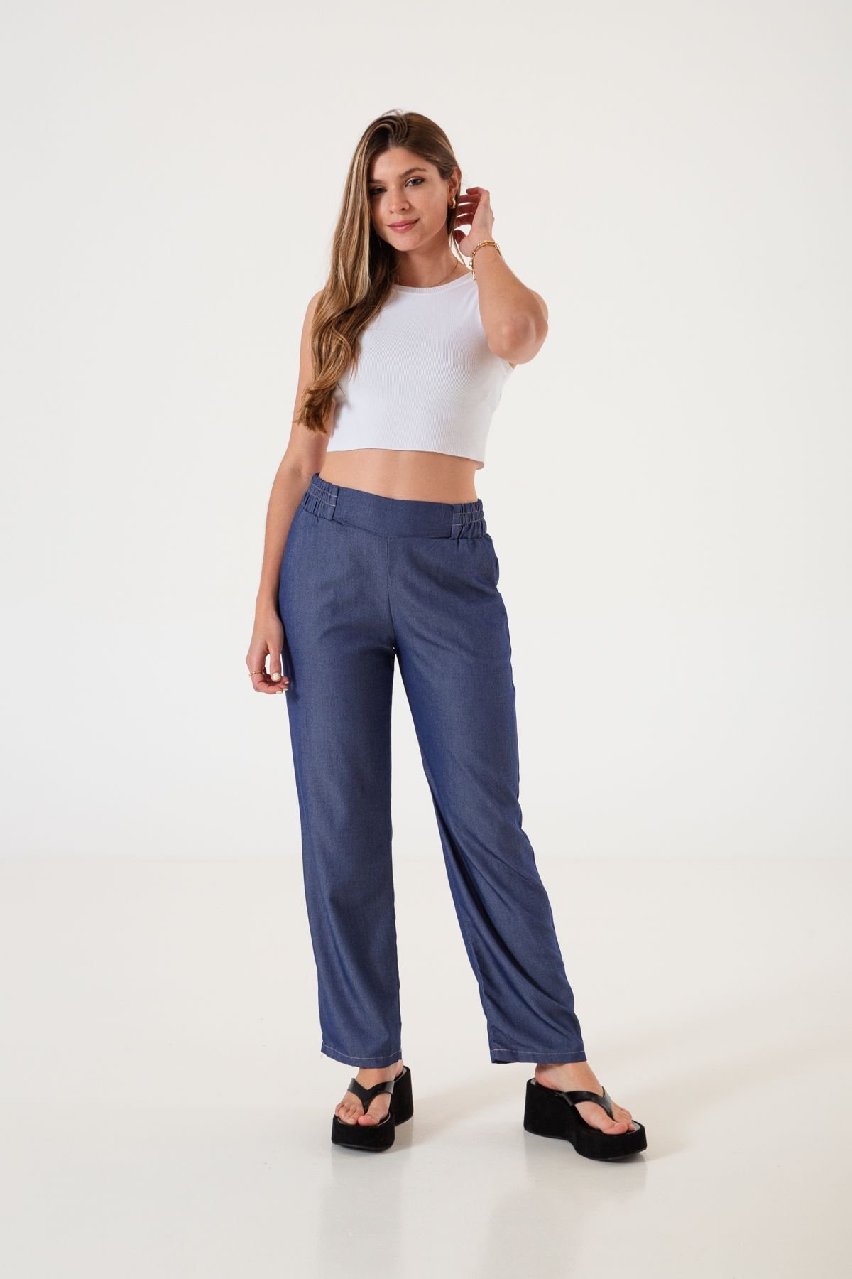 Mujer sonriendo luciendo pantalón recto de twill azul con sandalias negras y crop top blanco.