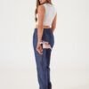 Mujer de espaldas con pantalón recto azul de twill liviano sosteniendo una flor, en ambiente minimalista.